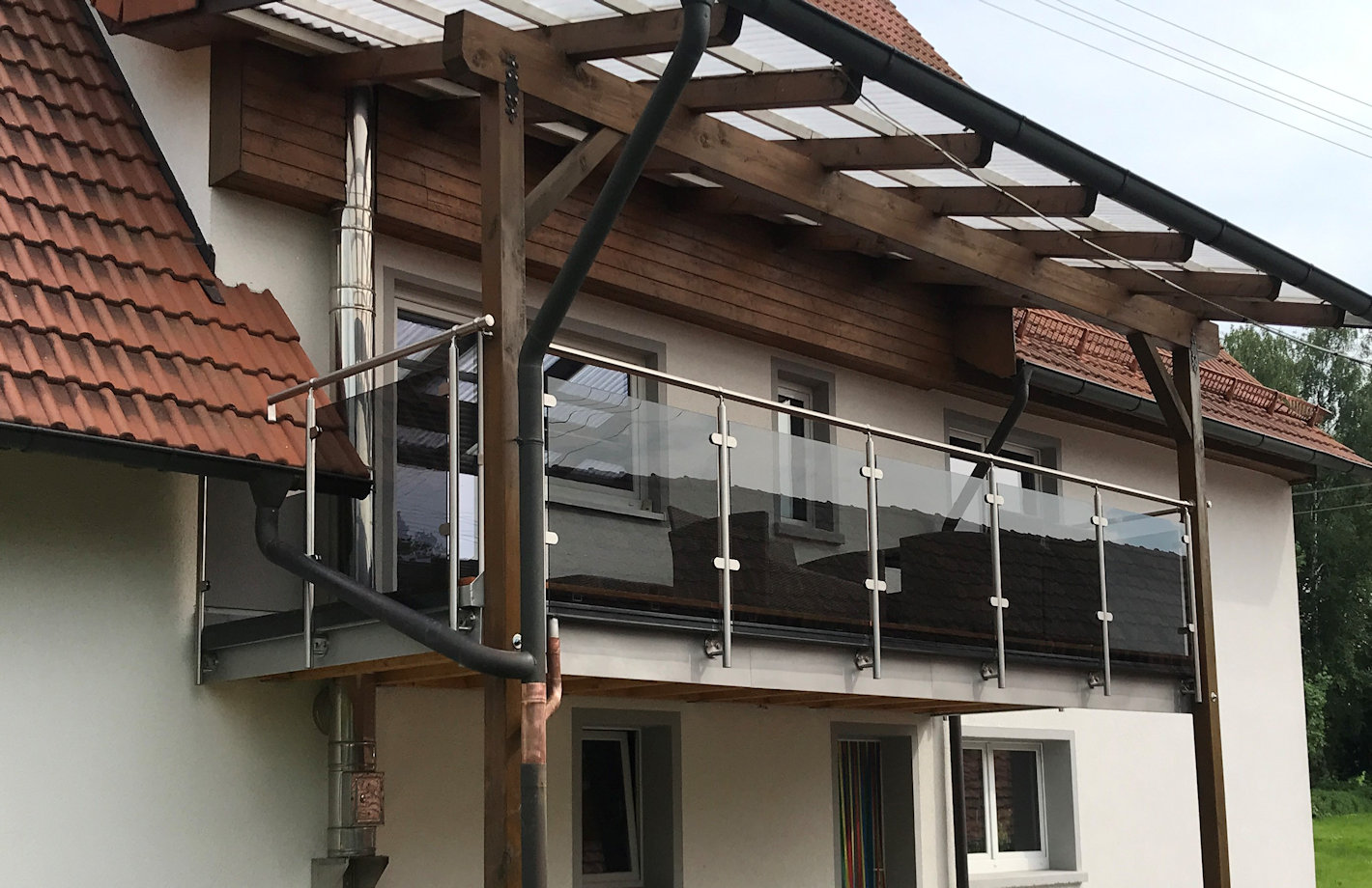 Balkongeländerbausatz aus Edelstahl und Grauglas zur vorgesetzten Montage an einen Holzbalkon